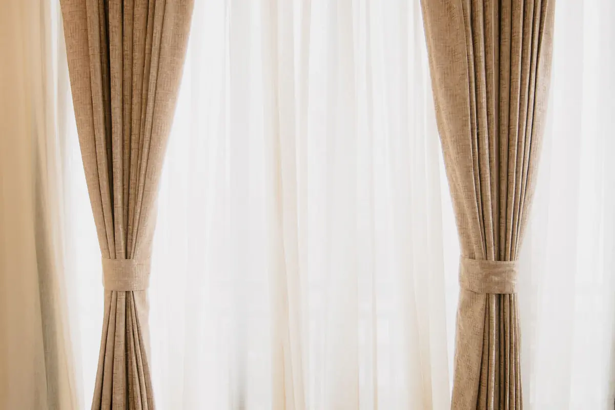 Cream curtains tied back over a sheer voile panel in a bright room