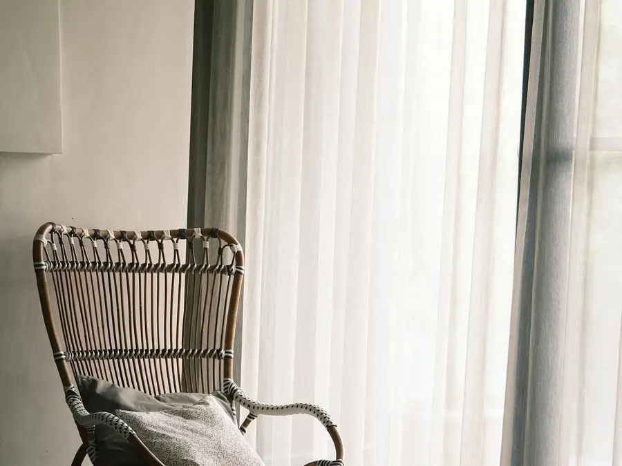 Sheer curtains filtering light beside a rattan armchair